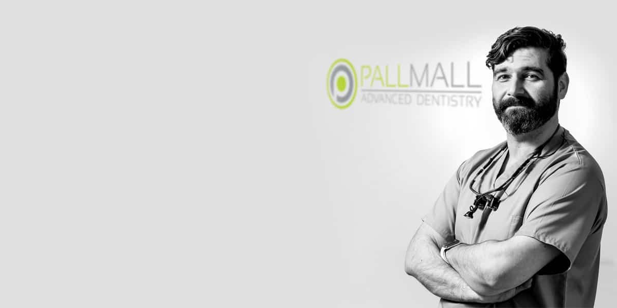 Dr Andrew Healy, arms folded, beside the Pall Mall Advanced Dentistry logo